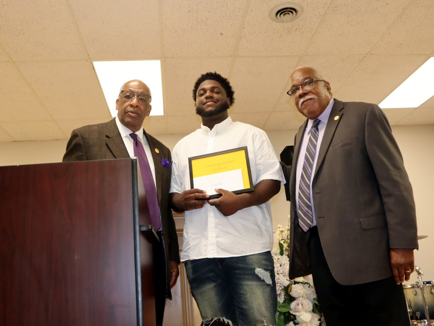 A scholarship recipient holding his award with Foundation directors